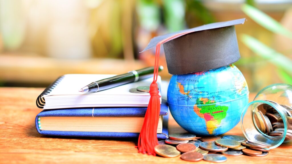 Graduation cap on a globe with books, pen and coins